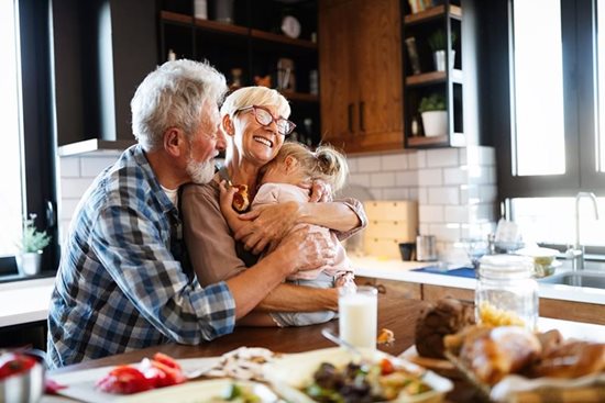 Bedsteforældre sidder i køkkenet med deres barnebarn og har en hyggelig stund, med kram og smil